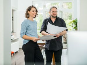 Zwei Mitarbeitende stehen im Büro und schauen sich ausgedruckte Plakate an